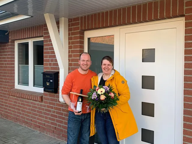 Ein Paar mit Blumenstrauß und Sekt vor der Haustür